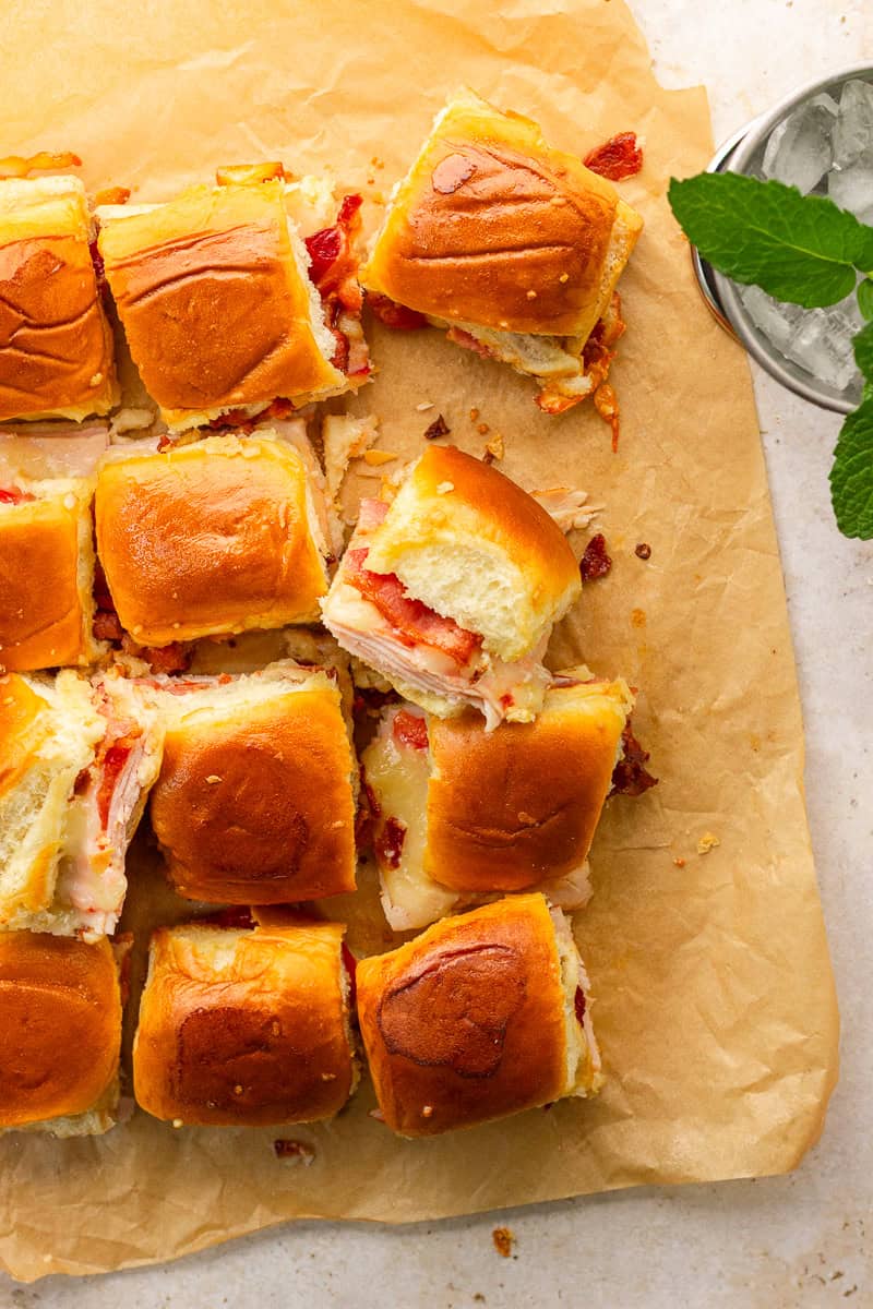 Cut hot brown sliders arranged on parchment paper with golden brown Hawaiian rolls and melted cheese.