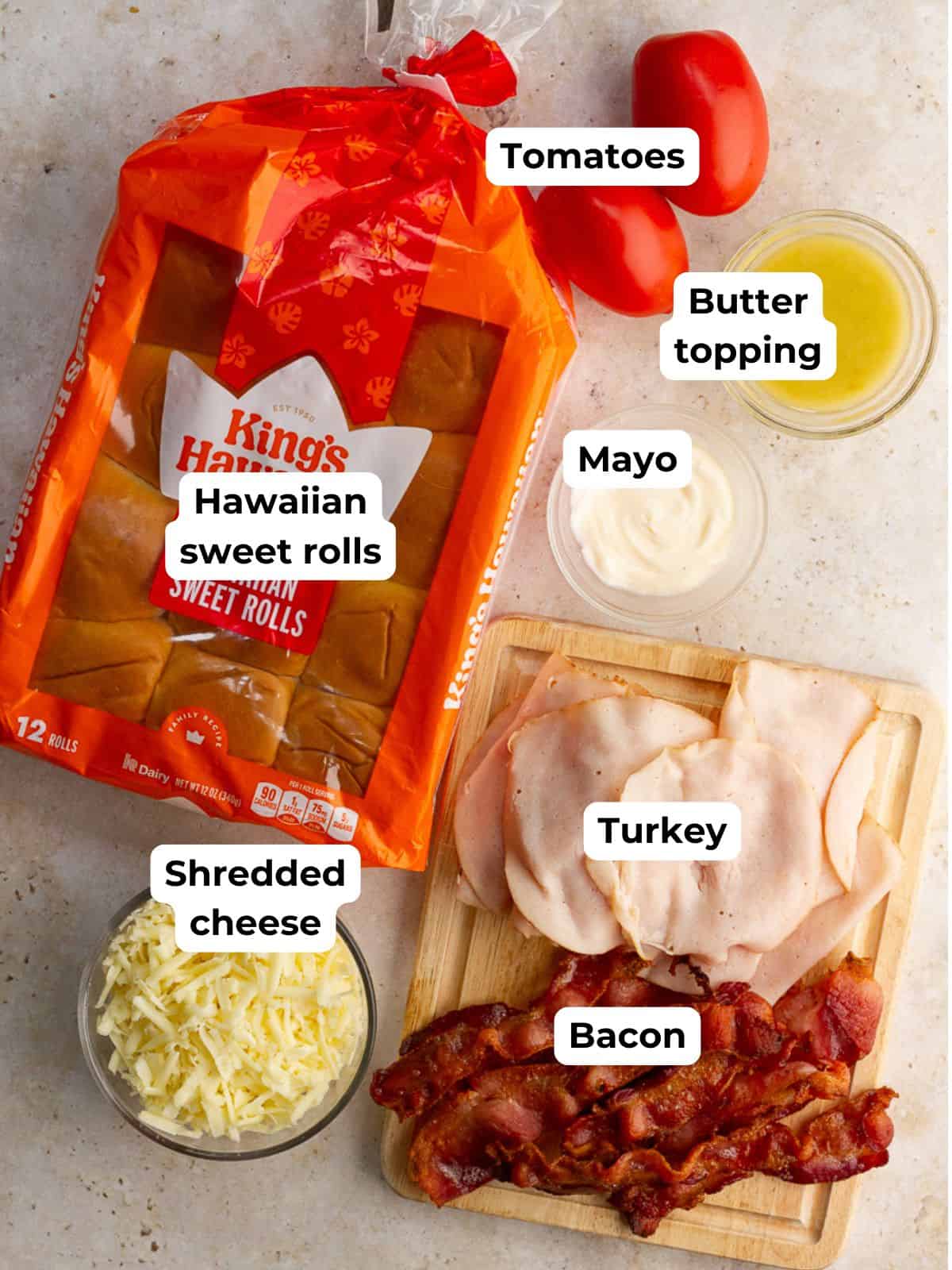 Ingredients for hot brown sliders including Hawaiian rolls, turkey, bacon, tomatoes, cheese, mayo, and butter topping.