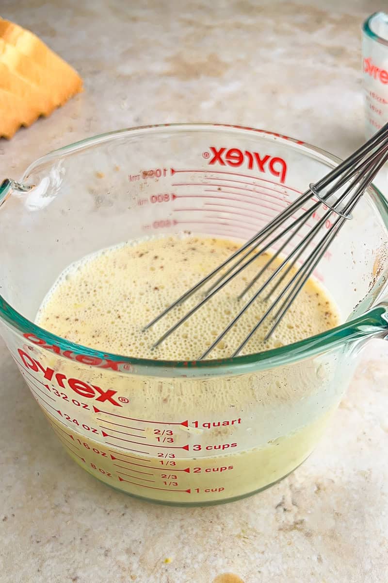 Whisked egg and milk custard with lemon and cinnamon in a glass measuring cup.