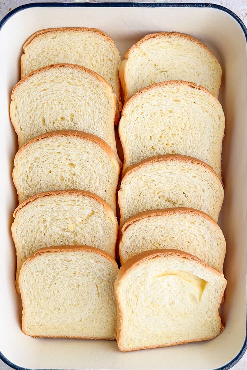 Sliced brioche bread arranged in overlapping layers in a 9x13 baking dish.
