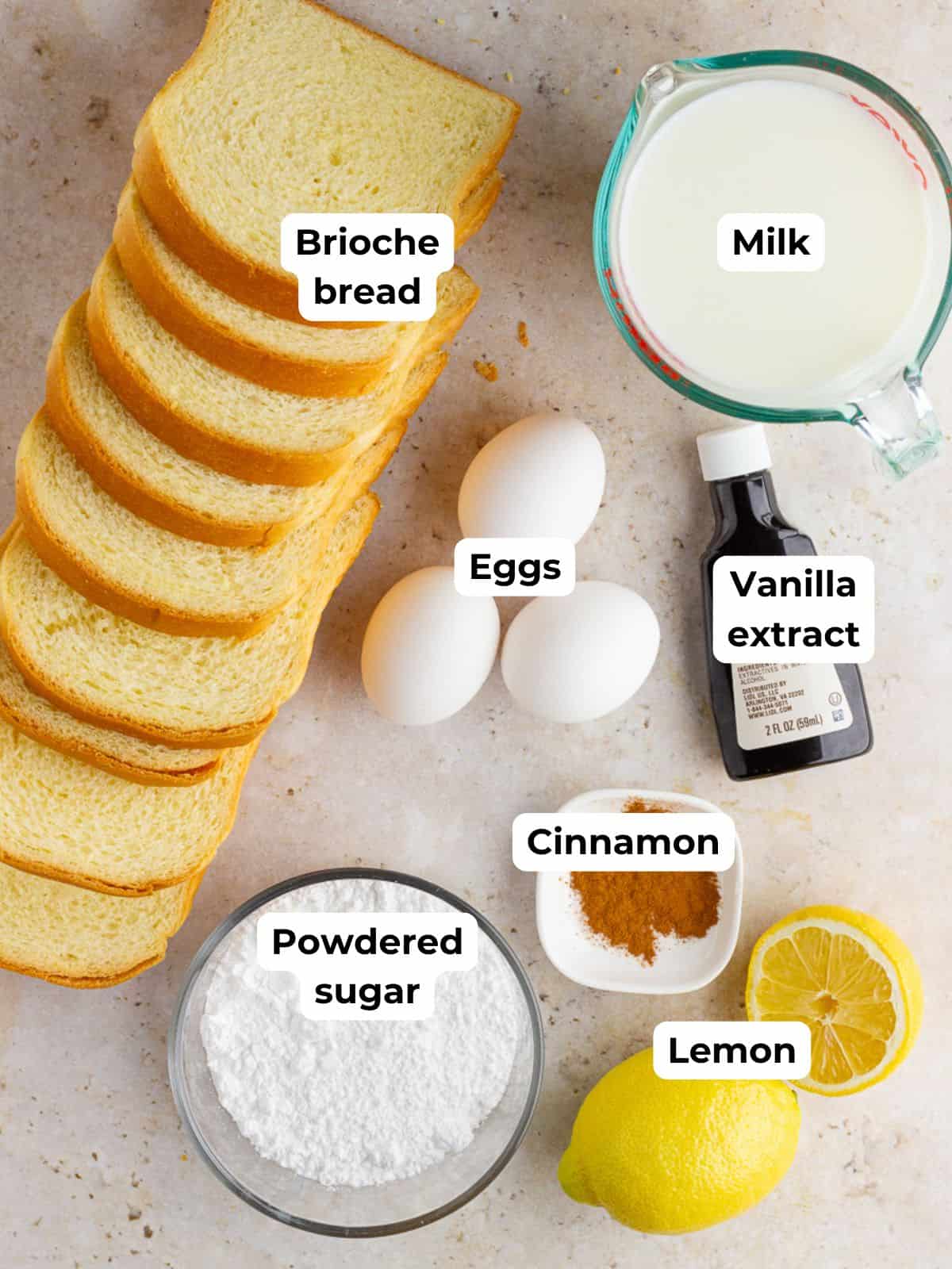 Ingredients for baked lemon french toast including brioche bread, eggs, milk, lemon, vanilla, cinnamon, and powdered sugar.
