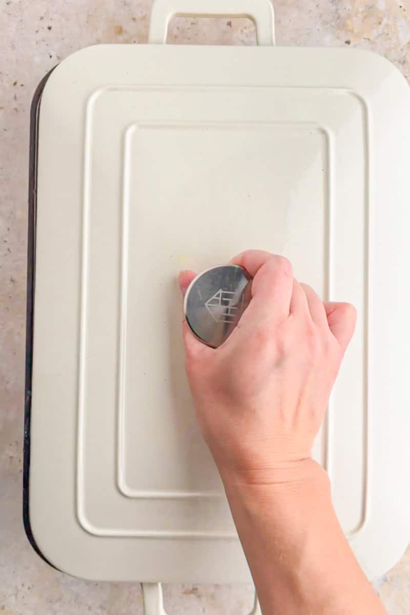Hand placing a lid on a baking dish to cover pesto chicken rice before baking.