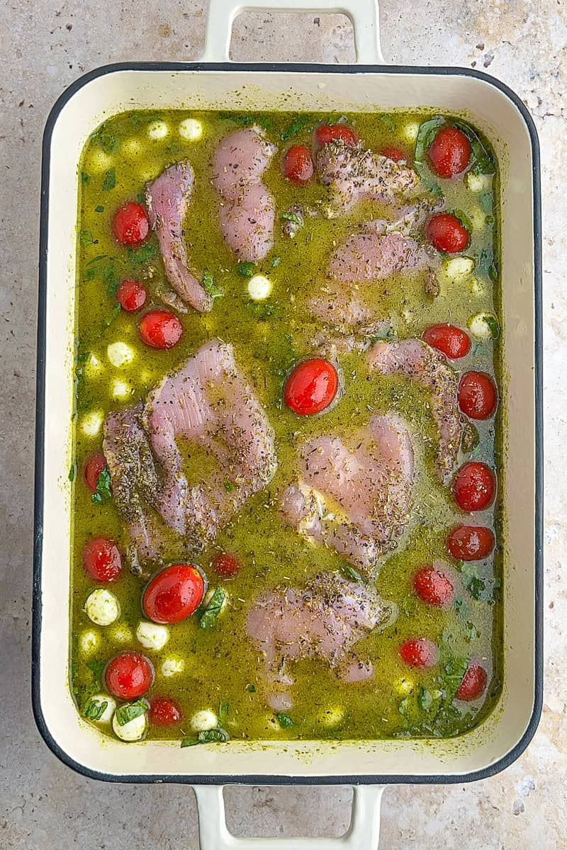 Seasoned chicken thighs placed on top of pesto rice with tomatoes and mozzarella in a baking dish.