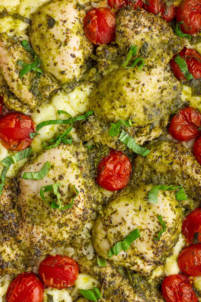 Close-up of baked pesto chicken thighs with melted mozzarella and roasted cherry tomatoes over rice.