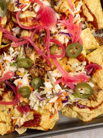 Featured image of pulled pork nachos with queso, BBQ sauce, coleslaw, jalapeños, and pickled onions.