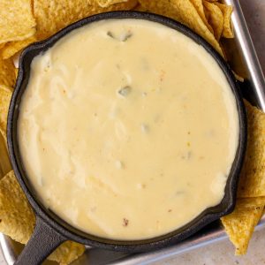 A small skillet filled with smooth, creamy spicy queso surrounded by tortilla chips.