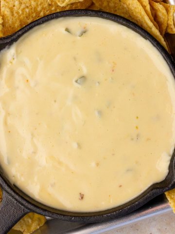 A small skillet filled with smooth, creamy spicy queso surrounded by tortilla chips.