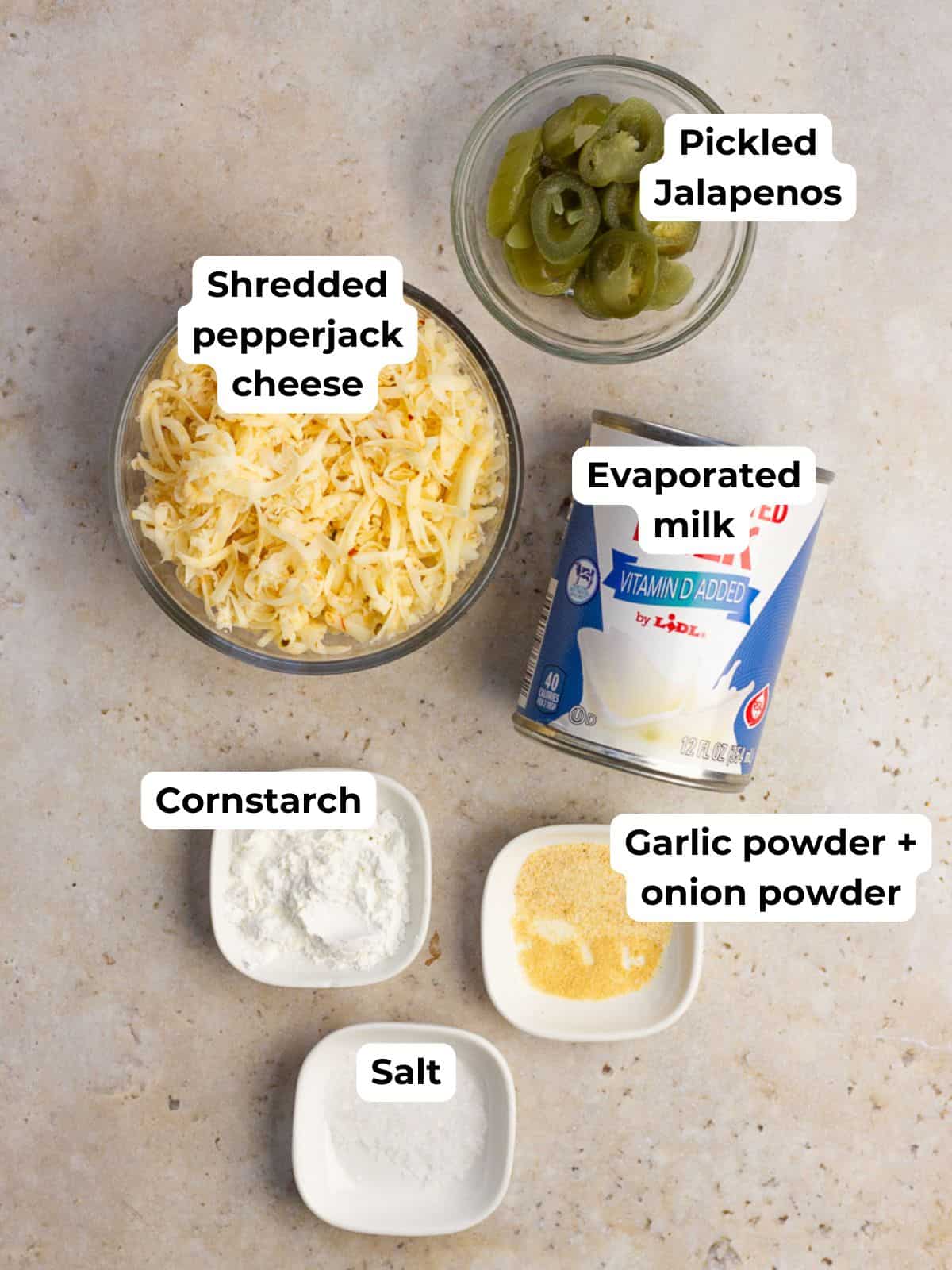 Ingredients for spicy queso including shredded pepper jack cheese, pickled jalapeños, evaporated milk, cornstarch, and spices.