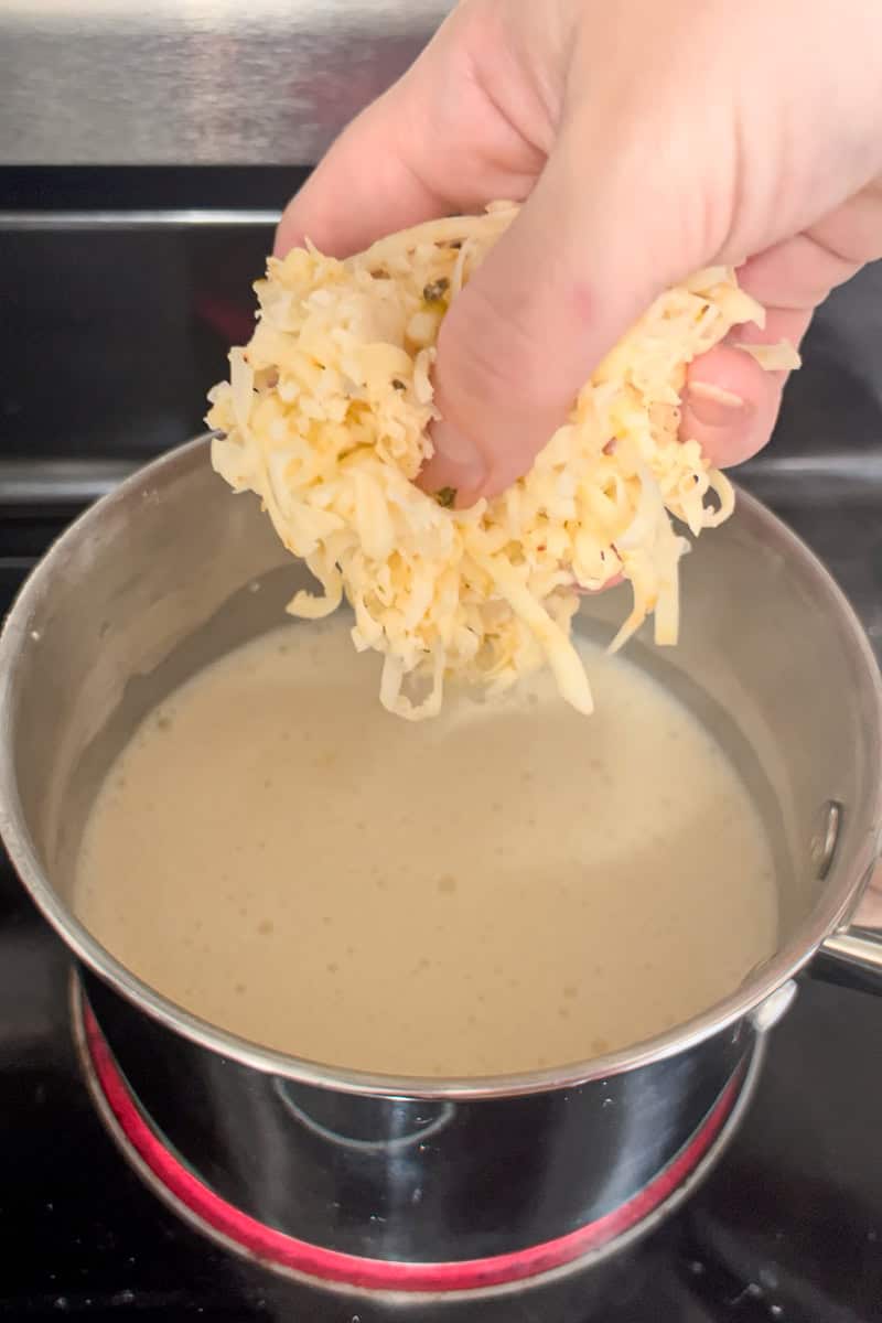 Freshly shredded pepper jack cheese being added to a saucepan with warm milk mixture.