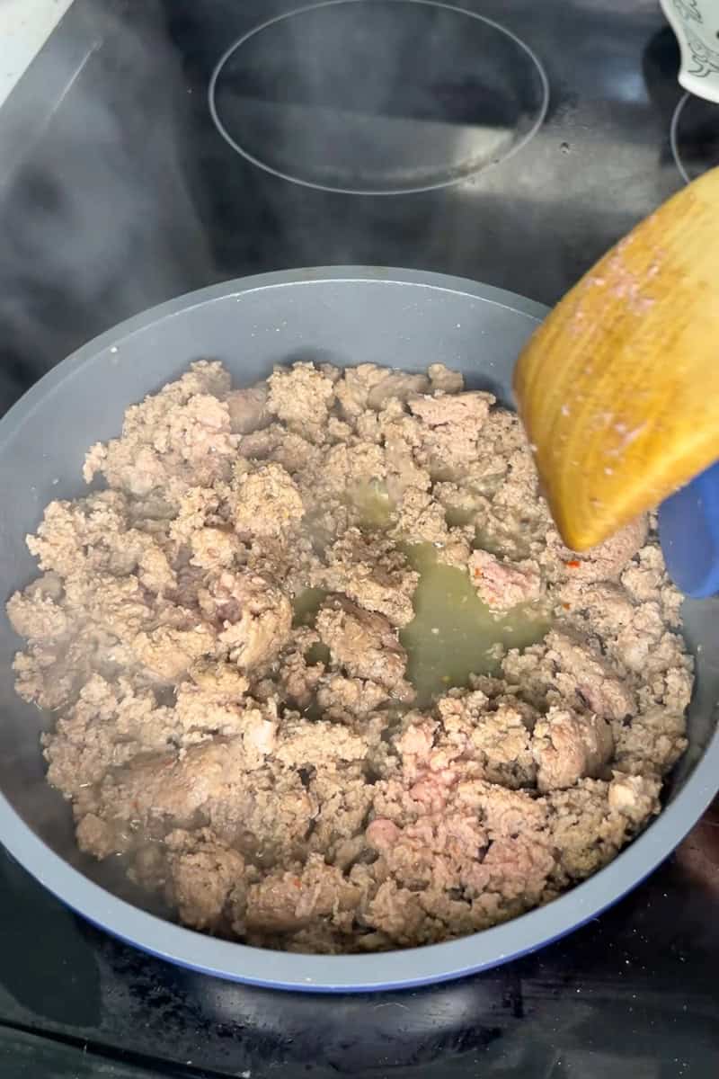 Ground sausage cooking in a skillet, browning and crumbling for the casserole filling.