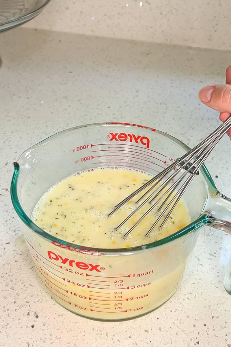 Egg mixture with milk and seasoning being whisked together for the breakfast casserole.