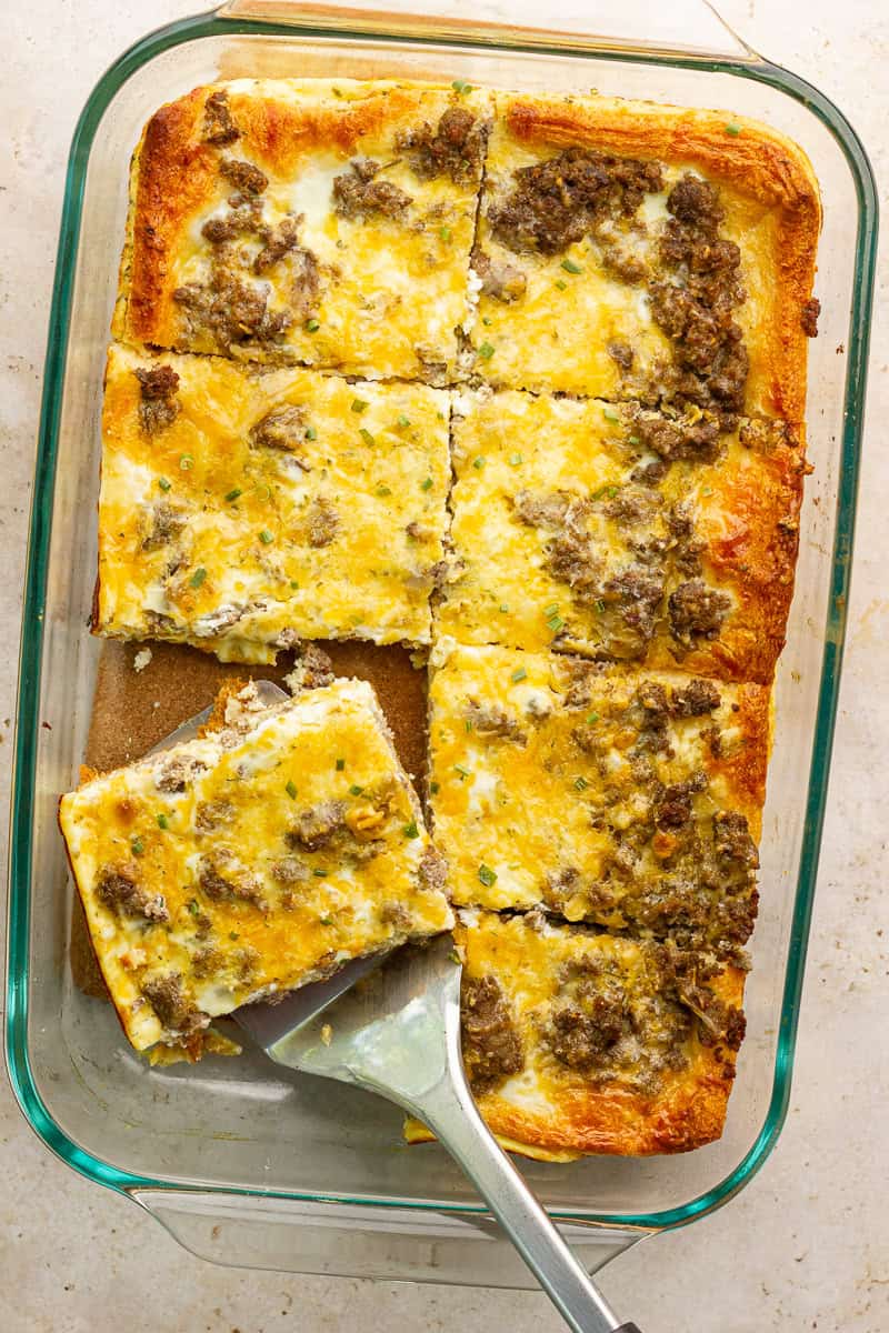 Breakfast casserole sliced into squares with a spatula lifting out a warm, cheesy serving.