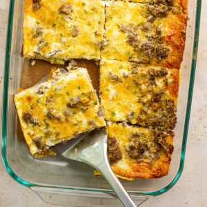 Breakfast casserole with crescent rolls sliced into squares with a spatula lifting out a cheesy, sausage-filled piece.