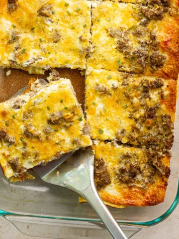 Breakfast casserole with crescent rolls sliced into squares with a spatula lifting out a cheesy, sausage-filled piece.