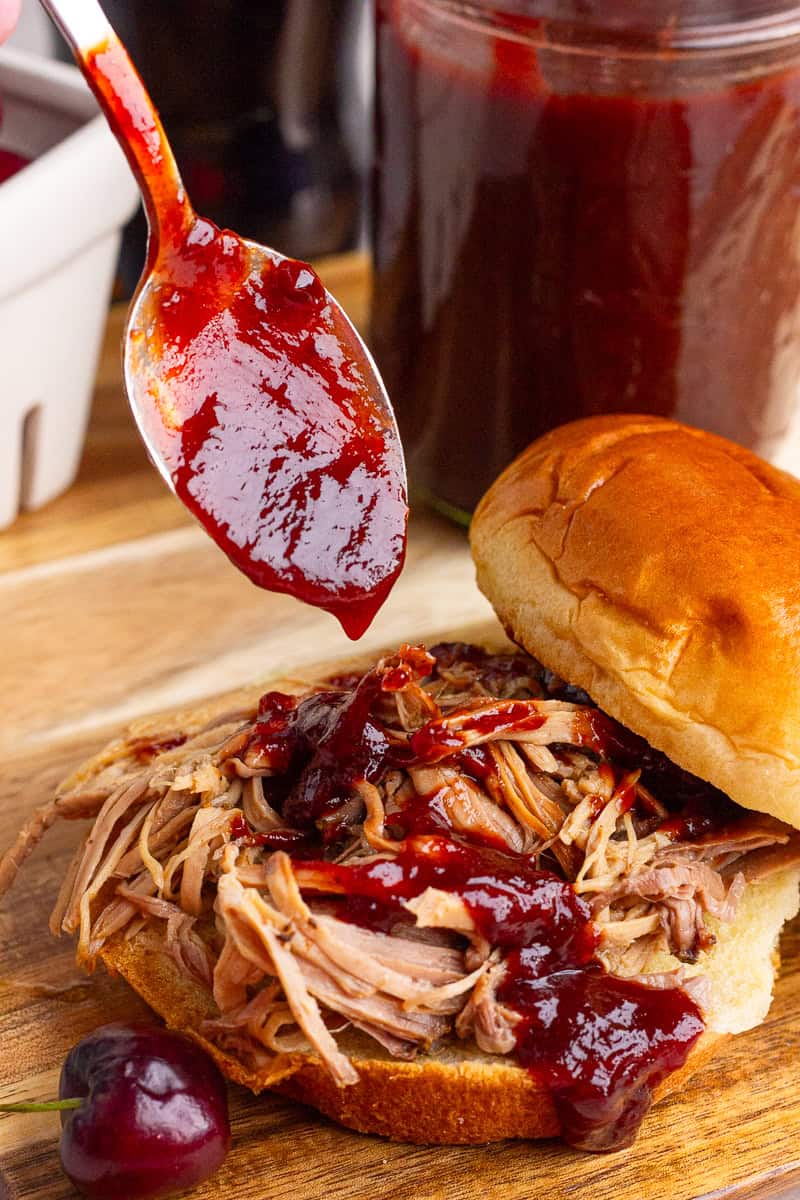 Cherry cola BBQ sauce is spooned over a pulled pork sandwich on a toasted bun.