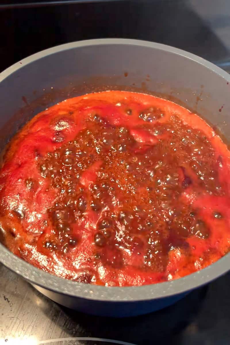 Cherry cola BBQ sauce bubbles in a saucepan as it thickens on the stove.