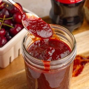 Thick cherry cola BBQ sauce drips from a spoon over a jar of sauce.
