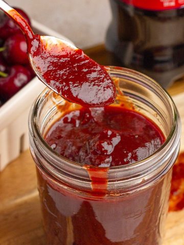Thick cherry cola BBQ sauce drips from a spoon over a jar of sauce.
