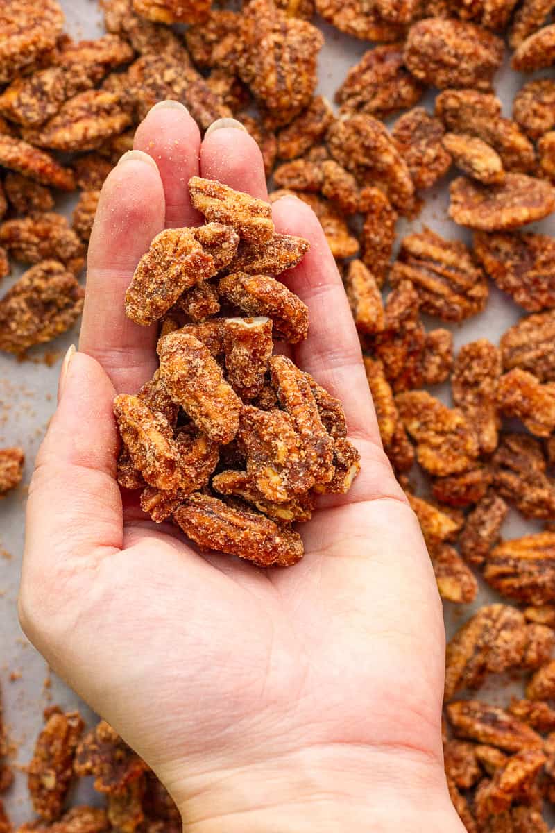A hand holds crunchy cinnamon sugar pecans over a sheet pan.