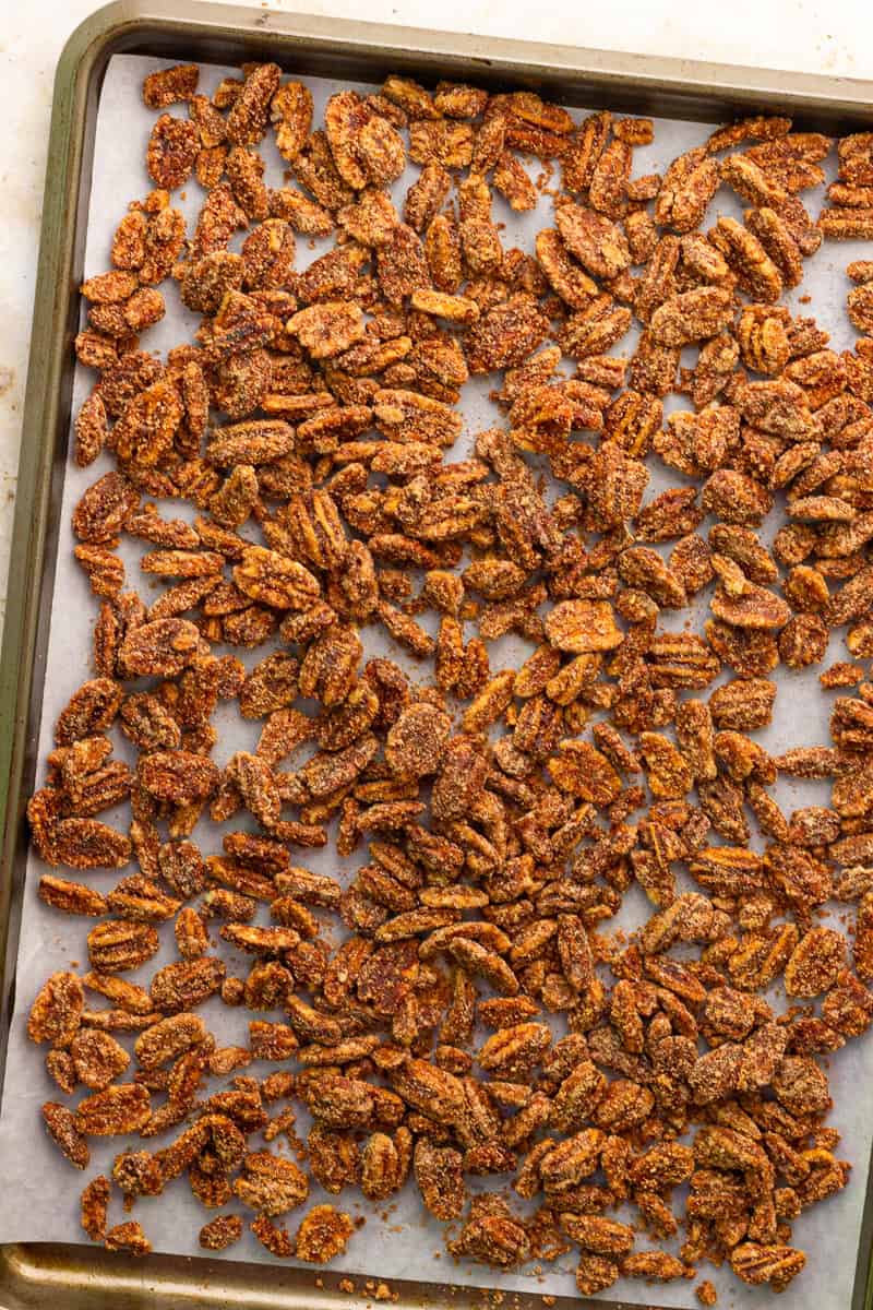 Cinnamon sugar pecans cool in a single layer on a parchment-lined sheet pan.