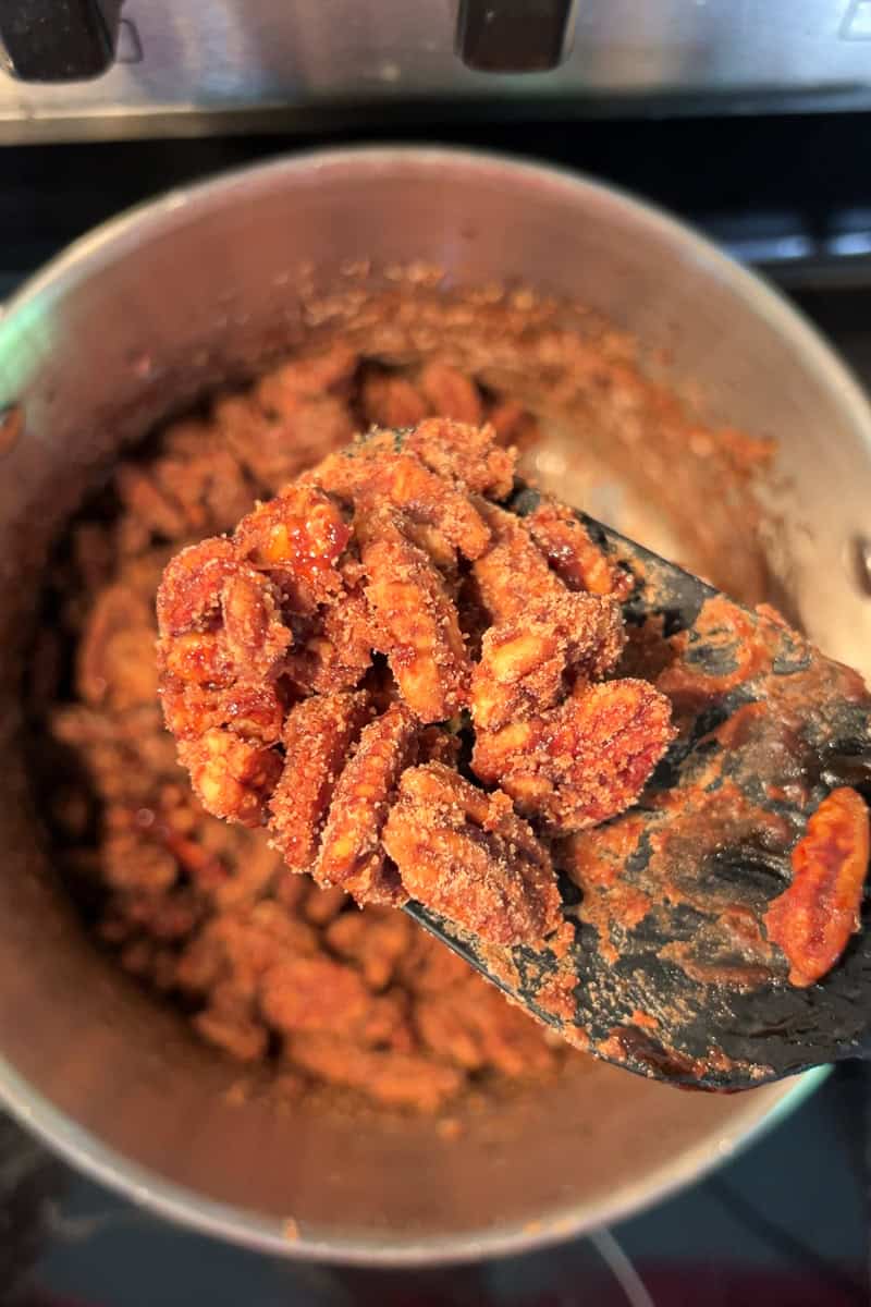 A spatula lifts crystallized cinnamon pecans from the pot.