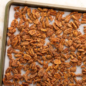 Cinnamon sugar pecans are spread across a parchment-lined sheet pan.