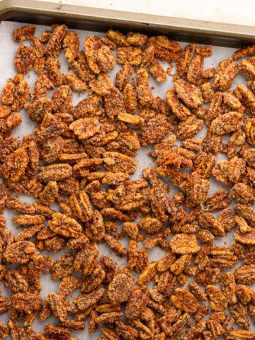 Cinnamon sugar pecans are spread across a parchment-lined sheet pan.