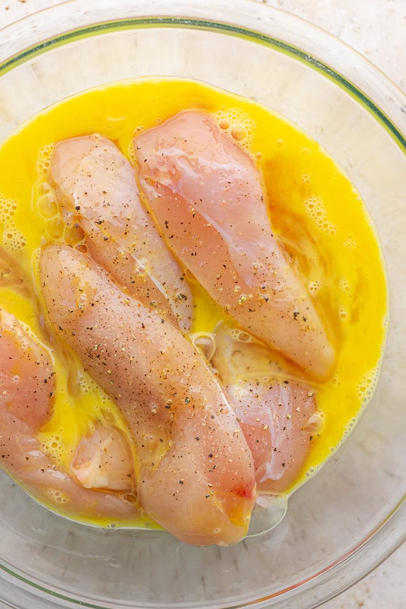 Chicken tenderloins sit in whisked eggs with salt and pepper before coating.