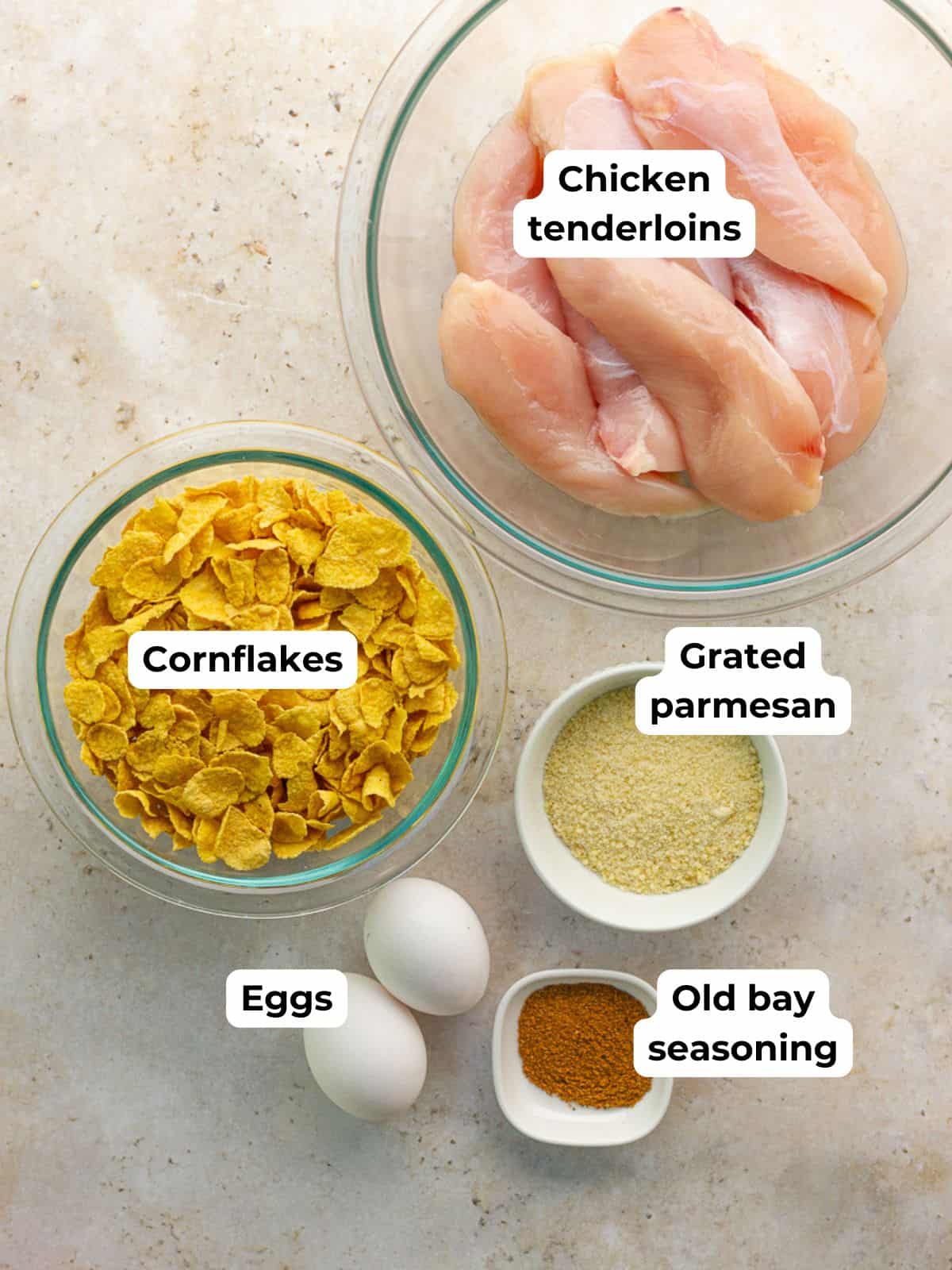 The main ingredients for cornflake chicken tenders are arranged in bowls and labeled.