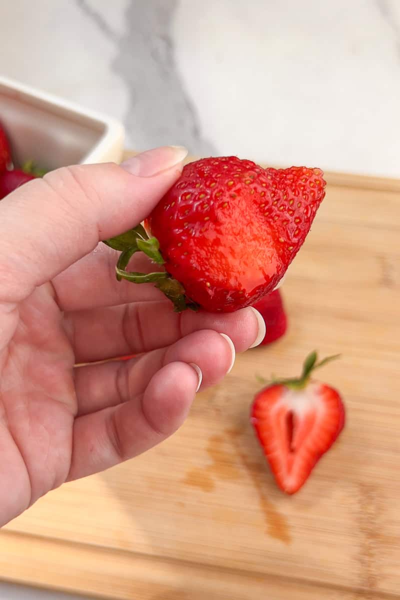 A hand holds a fresh strawberry after cutting a piece off the bottom.