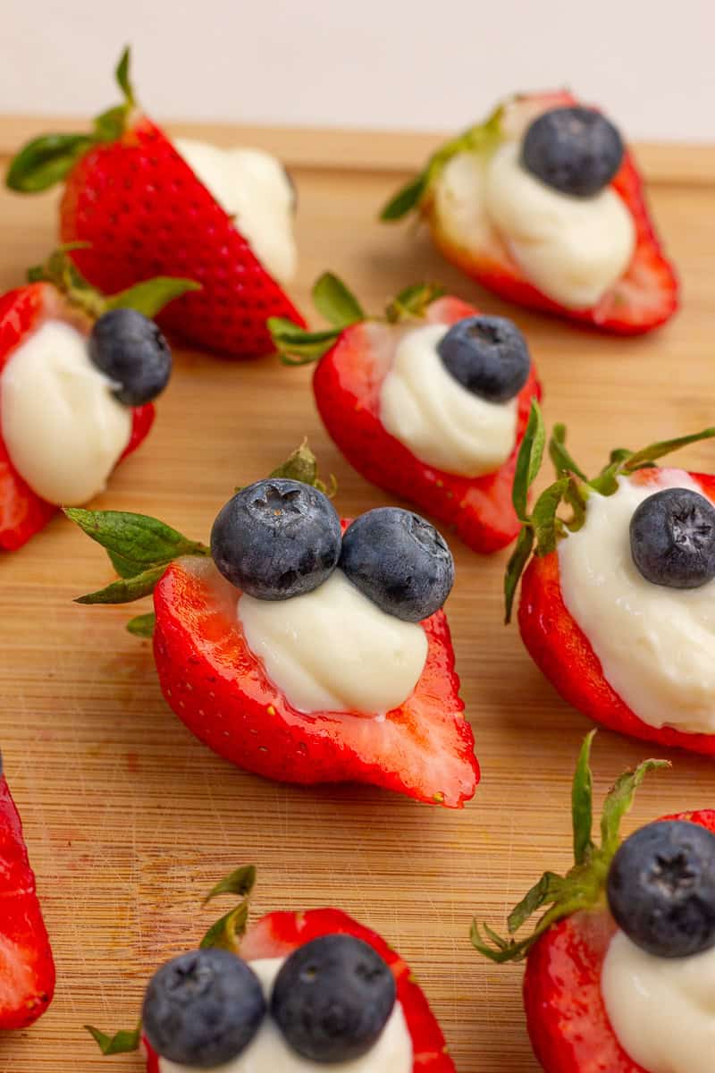 Deviled strawberries with cheesecake filling and blueberries sit on a wooden board.