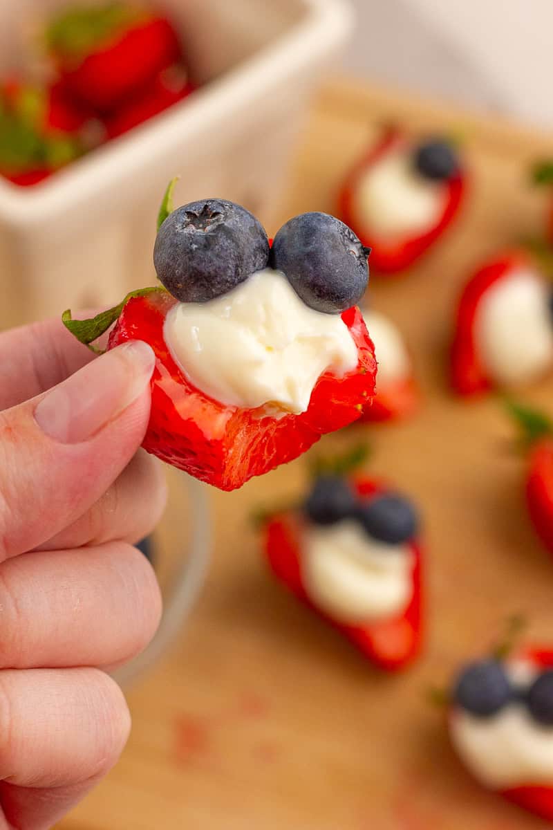 A bitten deviled strawberry shows the creamy cheesecake filling inside.