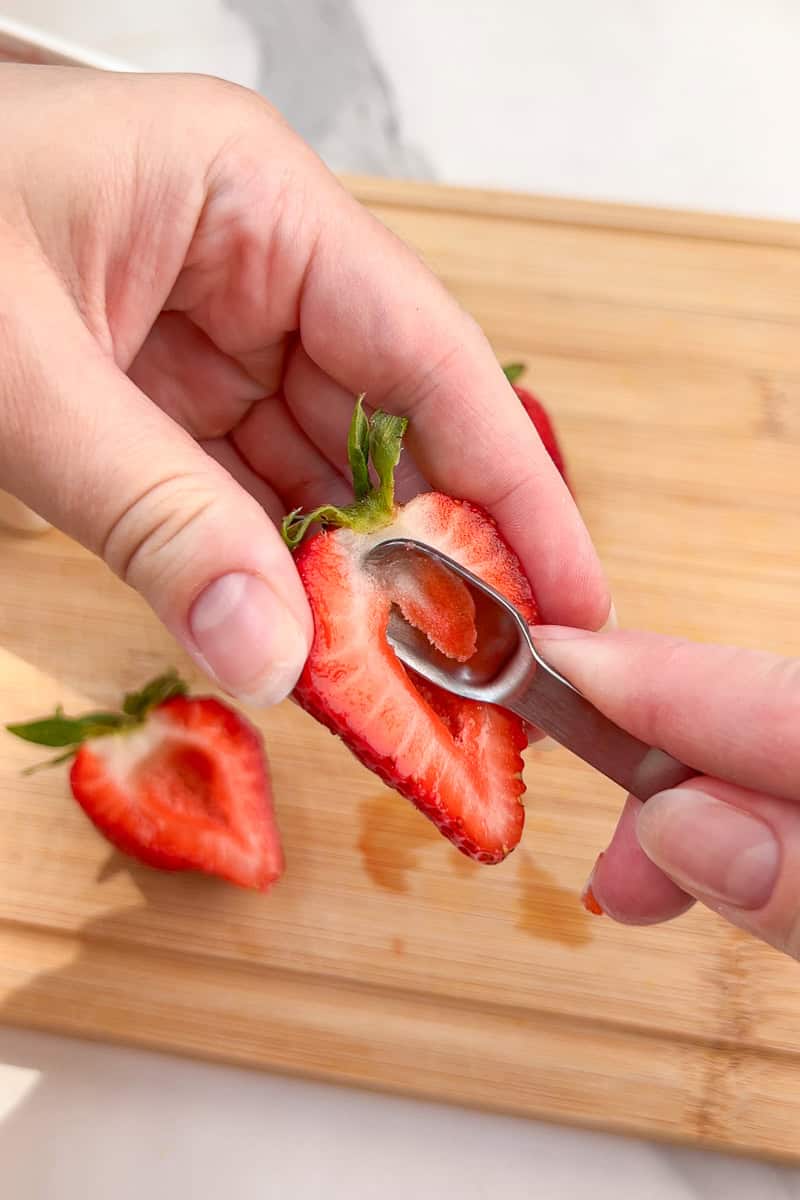 A small spoon scoops out the center of a sliced strawberry for deviled strawberries.