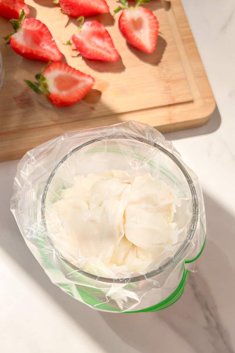 Cheesecake filling sits inside a zip-top bag ready for piping into strawberries.