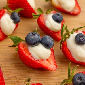 Deviled strawberries filled with cheesecake filling and topped with blueberries sit on a wooden board.