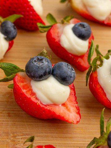 Deviled strawberries filled with cheesecake filling and topped with blueberries sit on a wooden board.