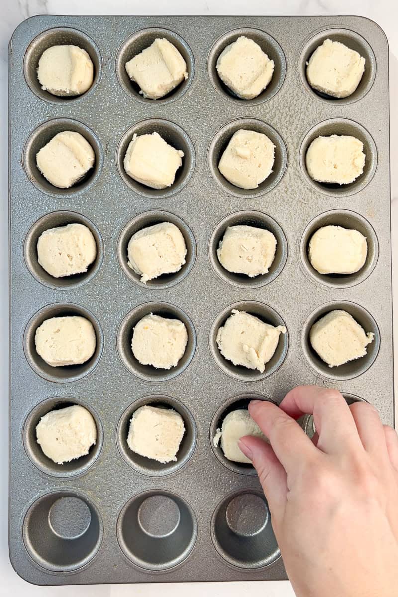 Sugar cookie dough pieces sit in a greased mini muffin pan before baking.