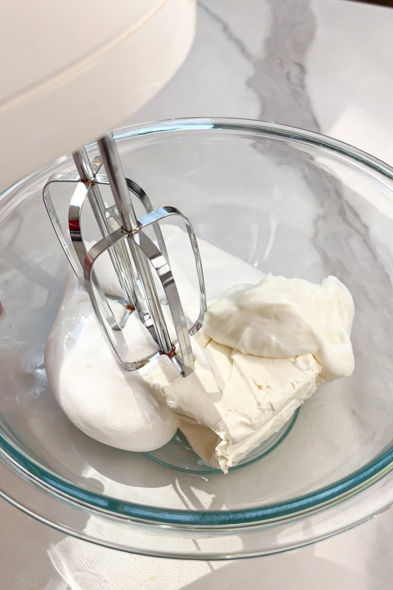 Marshmallow fluff, Greek yogurt, and Neufchâtel cheese mix together in a glass bowl.