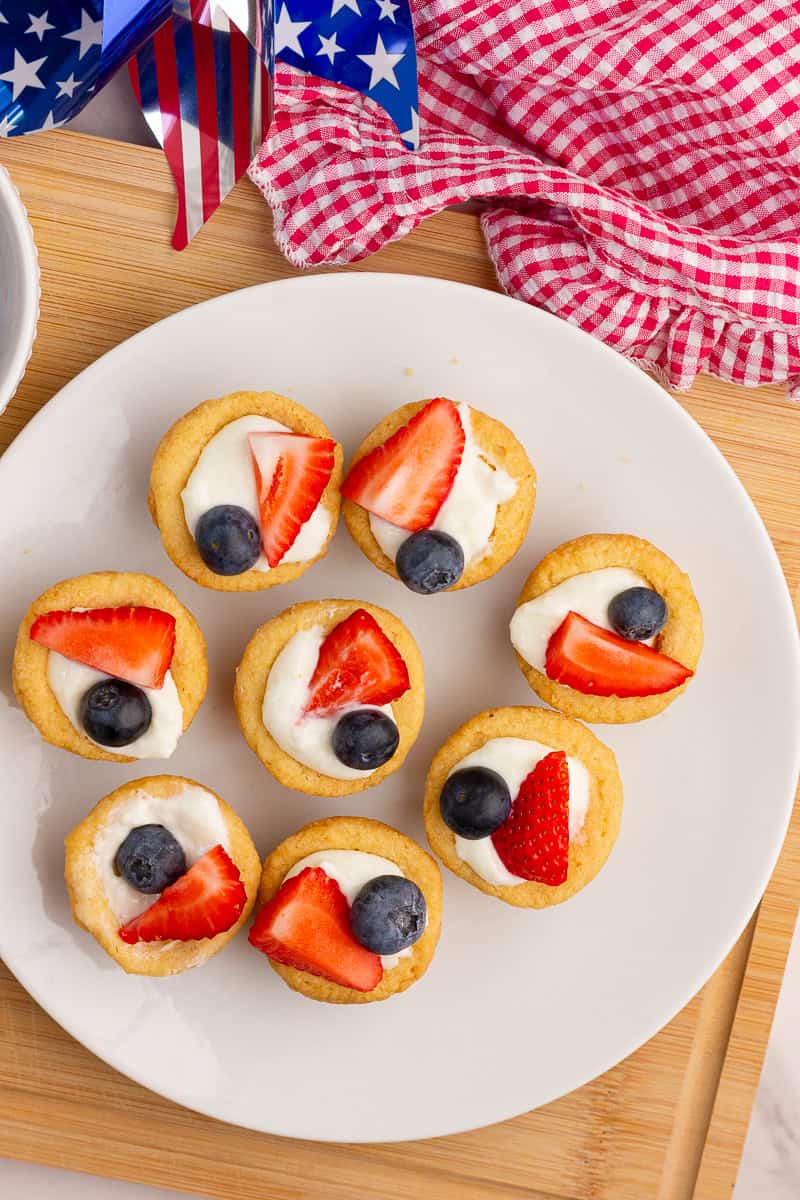 Red, white, and blue fruit pizza cups are arranged on a white serving plate.