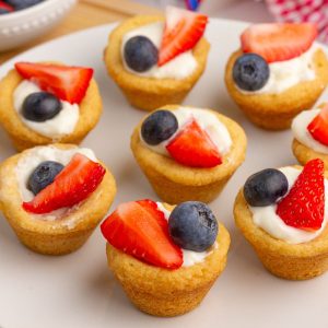 Fruit pizza cups with creamy filling, strawberries, and blueberries sit on a white plate.