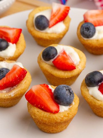 Fruit pizza cups with creamy filling, strawberries, and blueberries sit on a white plate.