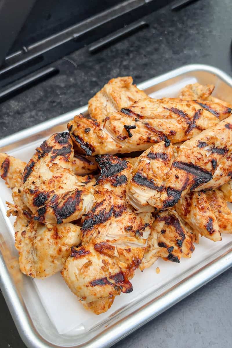 Freshly grilled honey mustard chicken tenders are held in a metal tray by the grill.