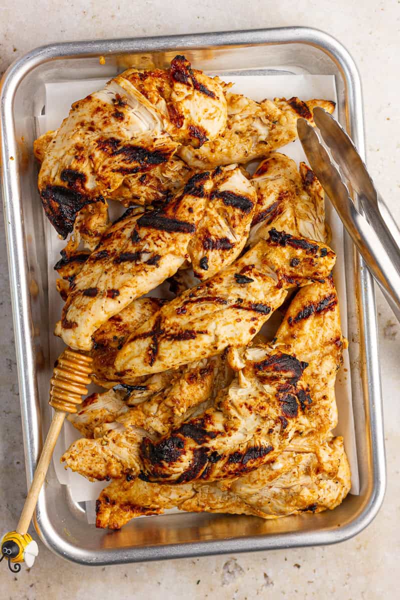 Grilled honey mustard chicken tenders are served in a metal tray with a honey dipper.