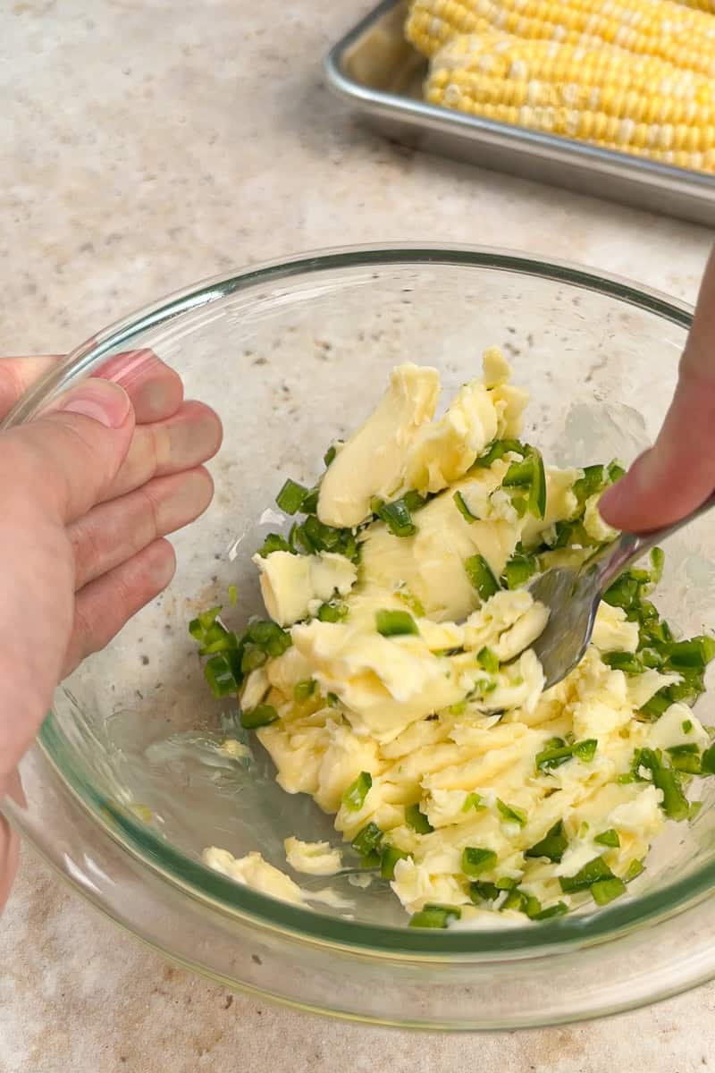 Softened butter and chopped jalapeños are mixed together in a glass bowl.