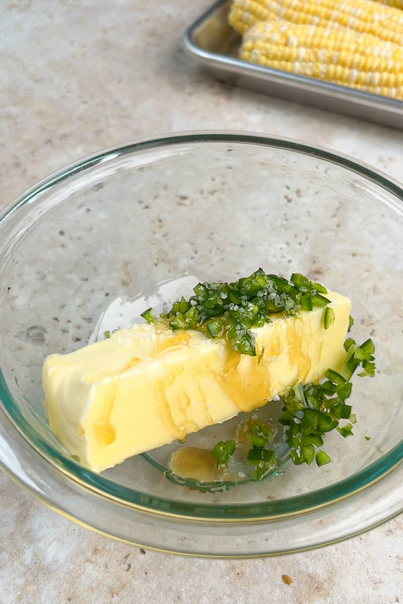 Butter, honey, salt, and chopped jalapeños are added to a glass bowl for jalapeno butter.