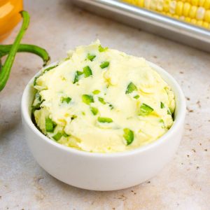 Jalapeno butter is served in a white bowl with fresh jalapeño and corn on the cob in the background.