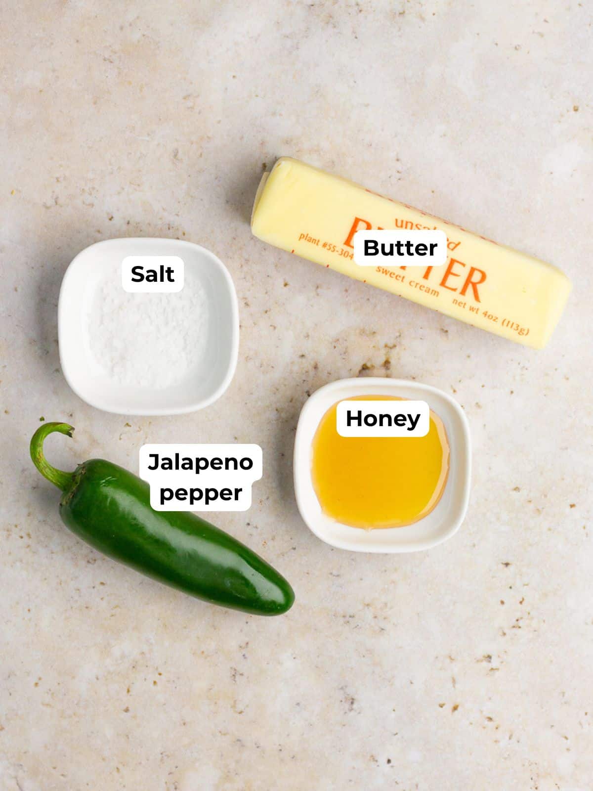 Butter, honey, salt, and a fresh jalapeno pepper are arranged on a countertop.