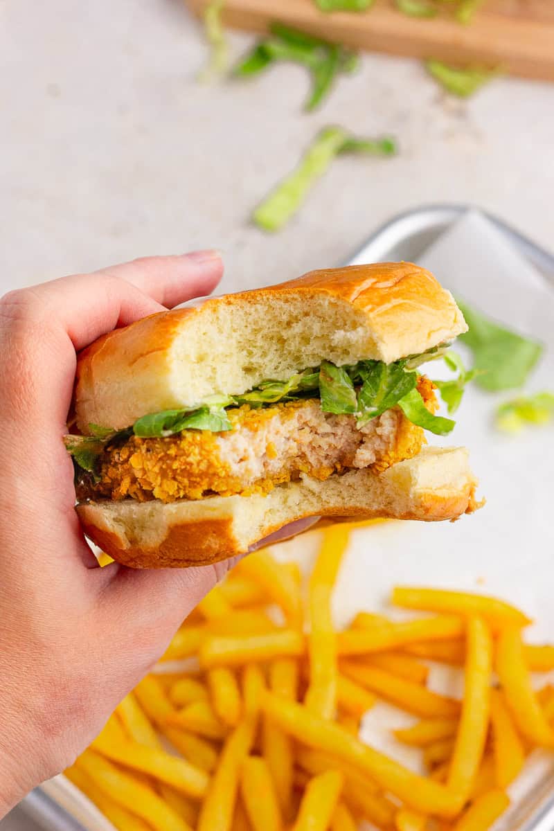 Bite taken out of a homemade McChicken sandwich showing the crispy cornflake chicken patty inside.
