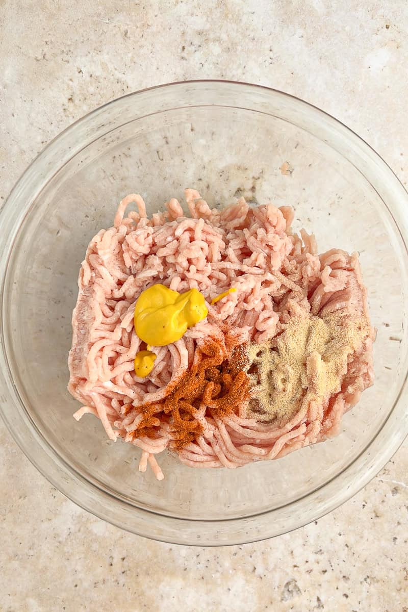 Ground chicken mixed with mustard and seasonings in a glass bowl for homemade McChicken patties.