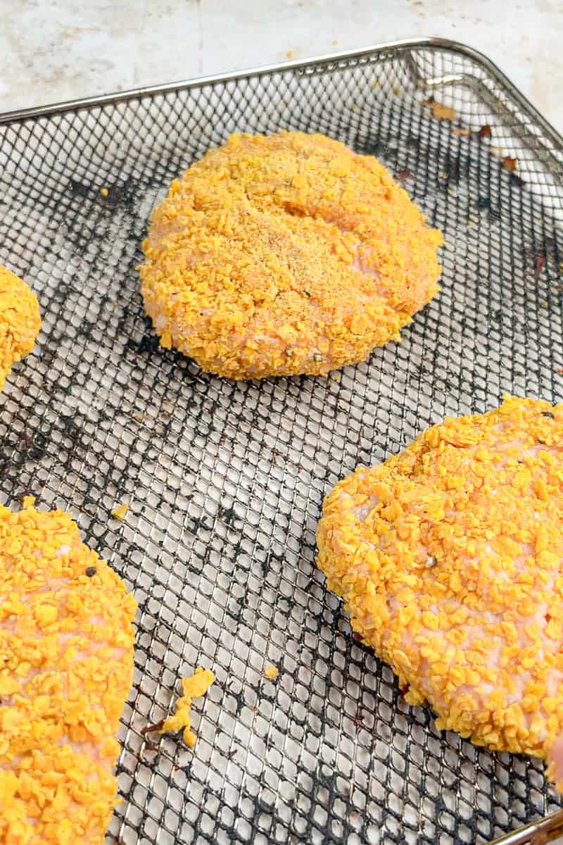 Cornflake-coated chicken patties resting on an air fryer tray before cooking.